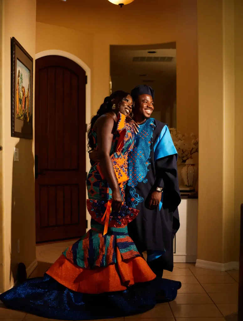 Couple embracing in a lamplit hallway, her kente train pooled at their feet