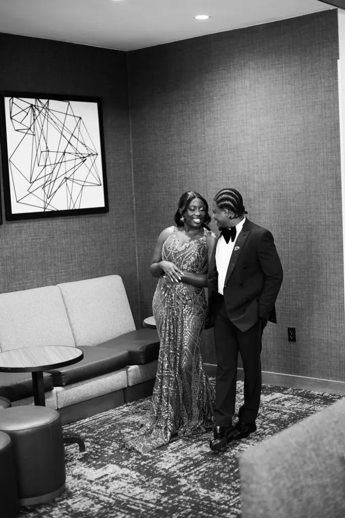 Black and white: couple in a sequinned gown and tuxedo sharing a quiet laugh in a lounge