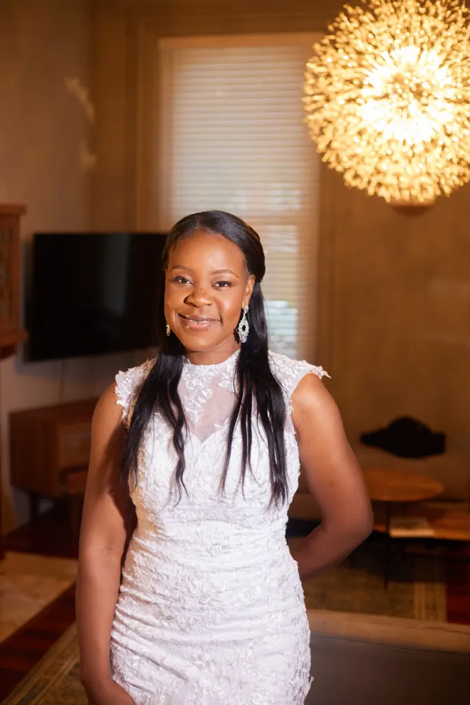 Bride in a high-neck lace gown smiling in a warm living room under a starburst light