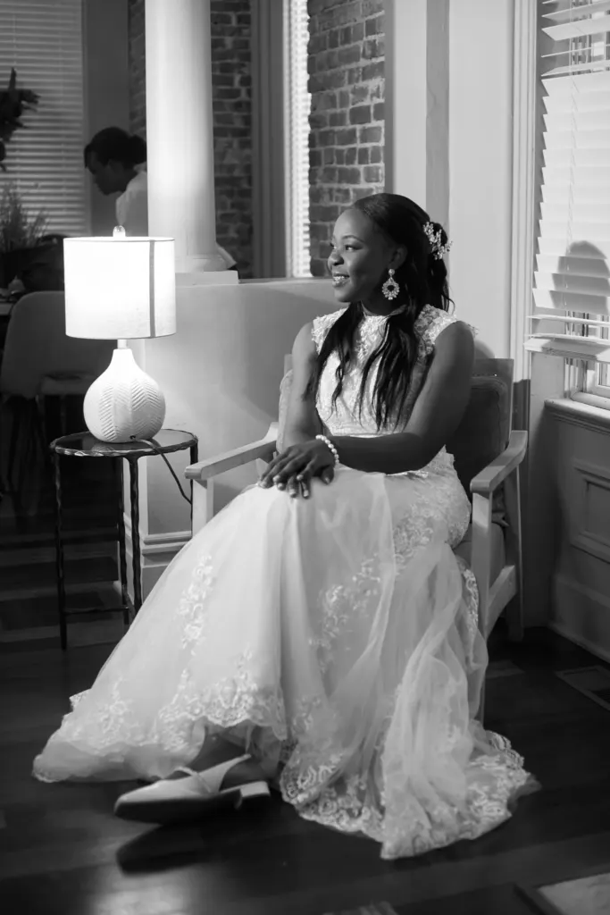 Black and white: bride seated by a lamp and tall windows, gown spread around her