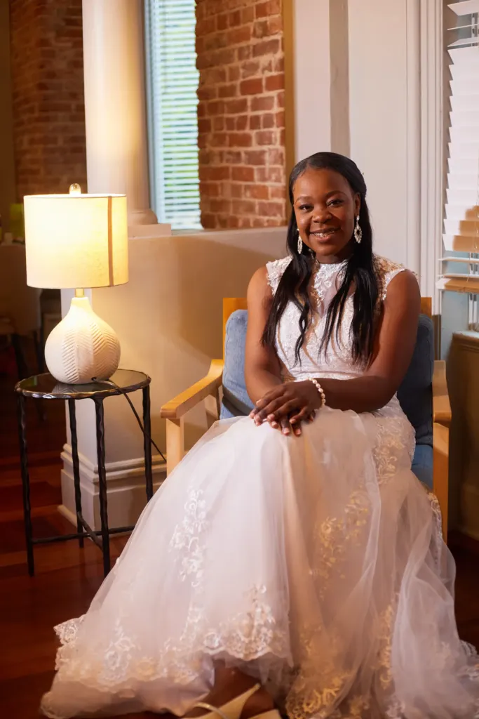 Bride seated in an armchair beside a glowing lamp, smiling at the camera