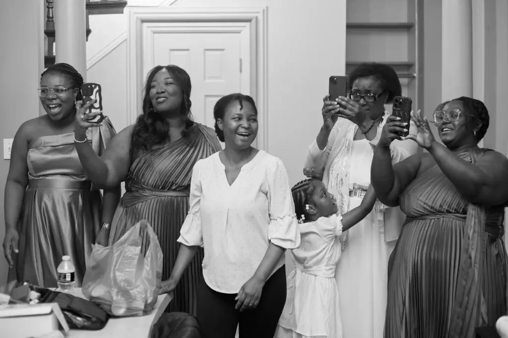 Black and white: family and bridesmaids laughing and filming the first look on their phones