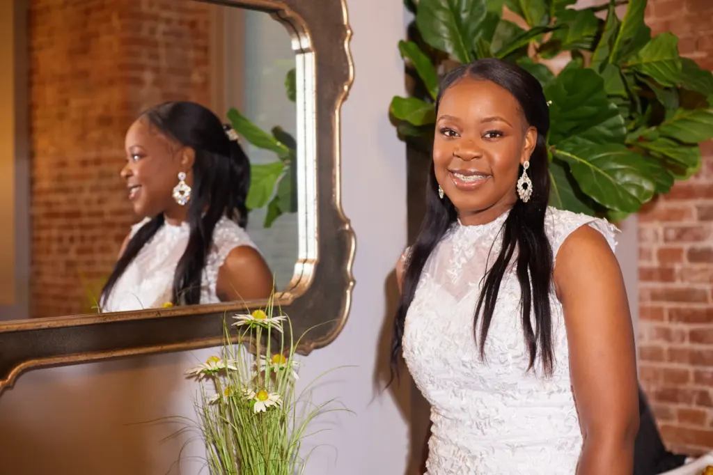 Bride beside a gilded mirror and a fiddle leaf fig, her reflection smiling back