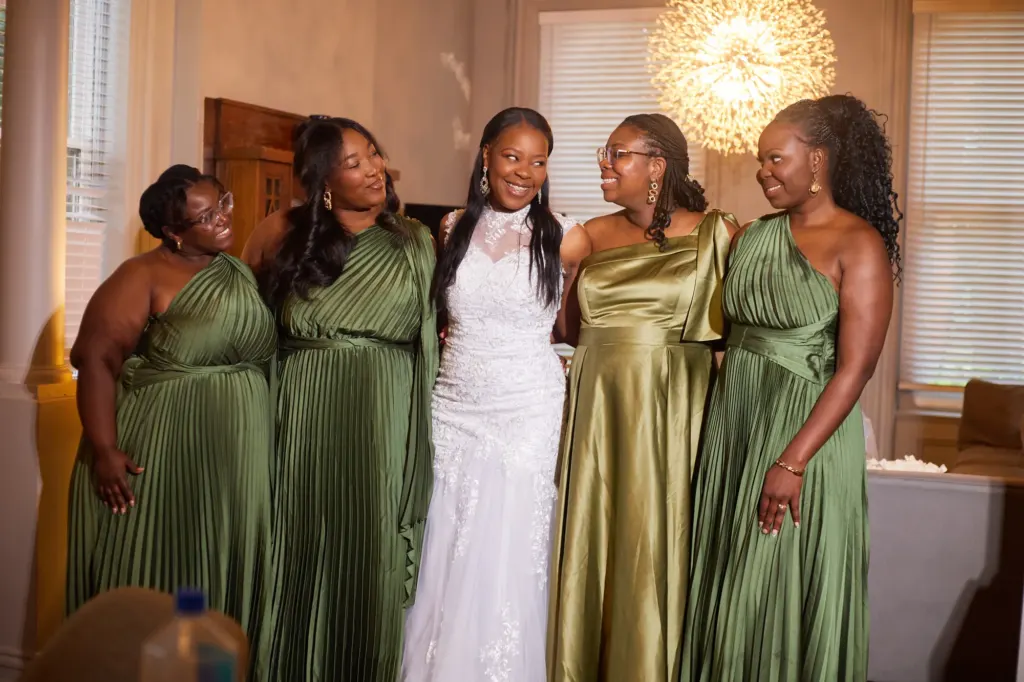 Bride in white laughing with four bridesmaids in sage and olive satin gowns