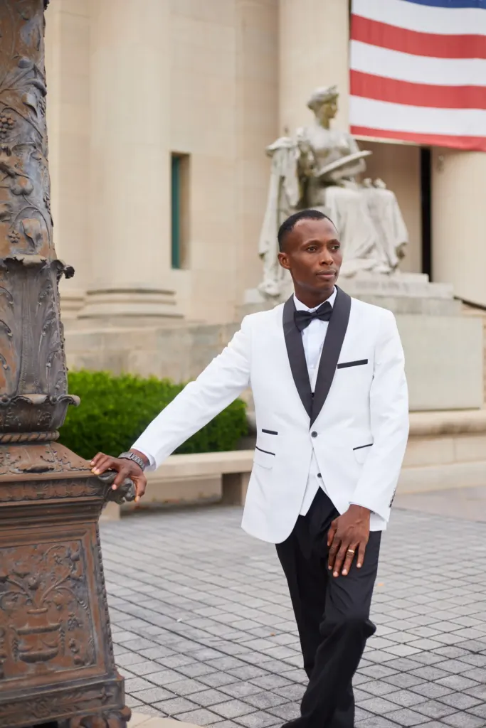 Groom in a white dinner jacket leaning on an ornate bronze lamppost