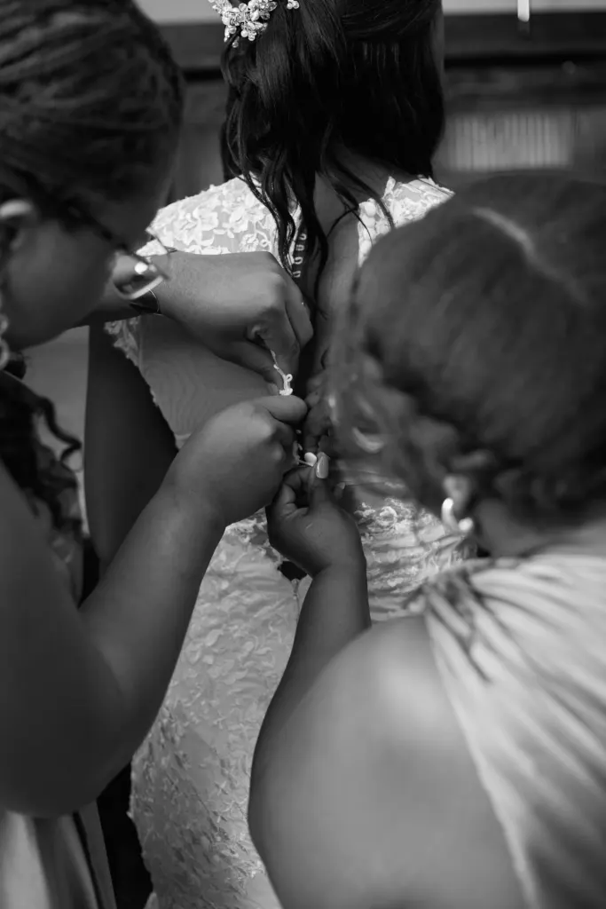 Black and white: hands fastening the buttons down the back of a lace wedding gown