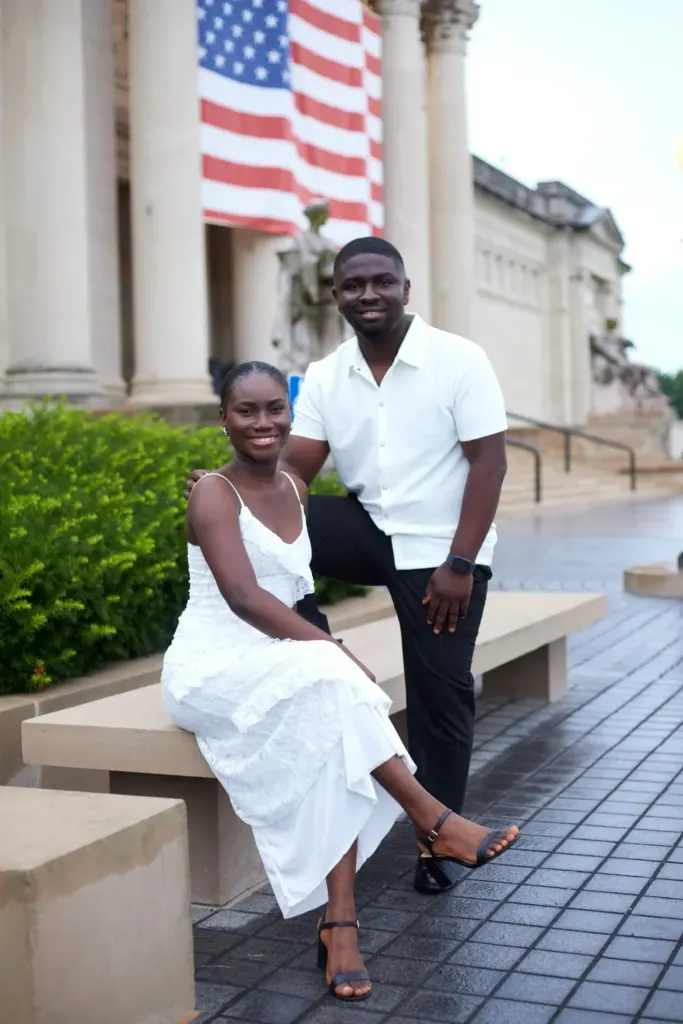 Couple seated on a stone bench before columned steps, smiling