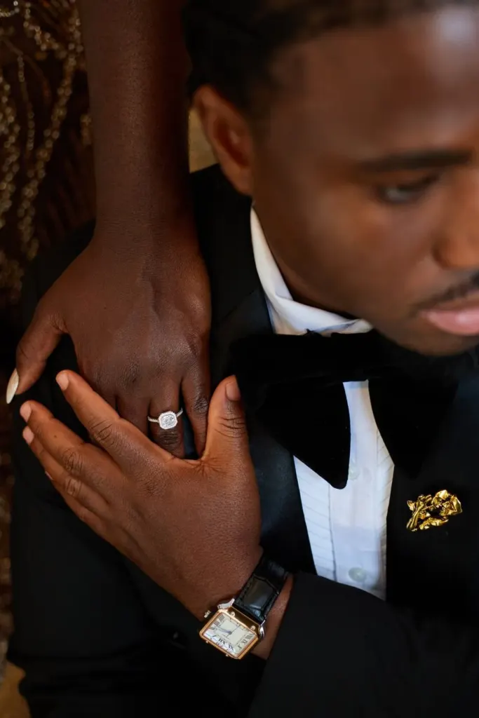Hands, engagement ring and watch against a black tuxedo