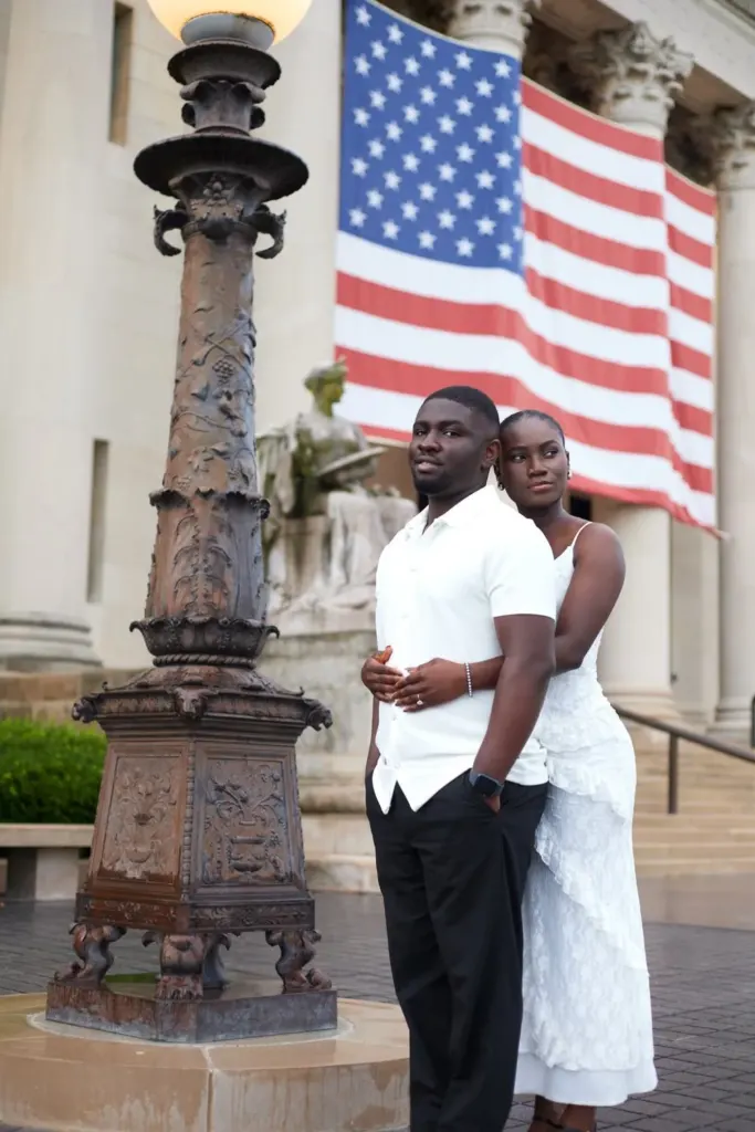 Couple standing beside a bronze lamppost in front of a flag-draped building