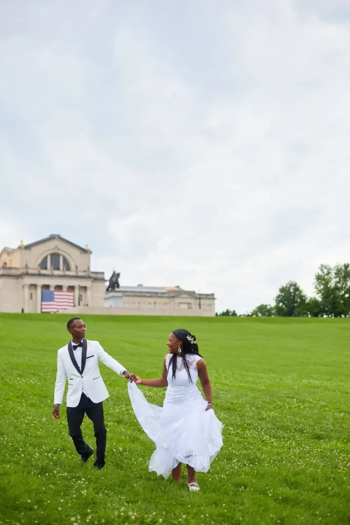 Bride and groom walking hand in hand across a green hillside, gown flowing