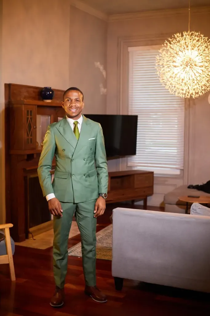 Groomsman in a sage double-breasted suit under a glowing pendant light