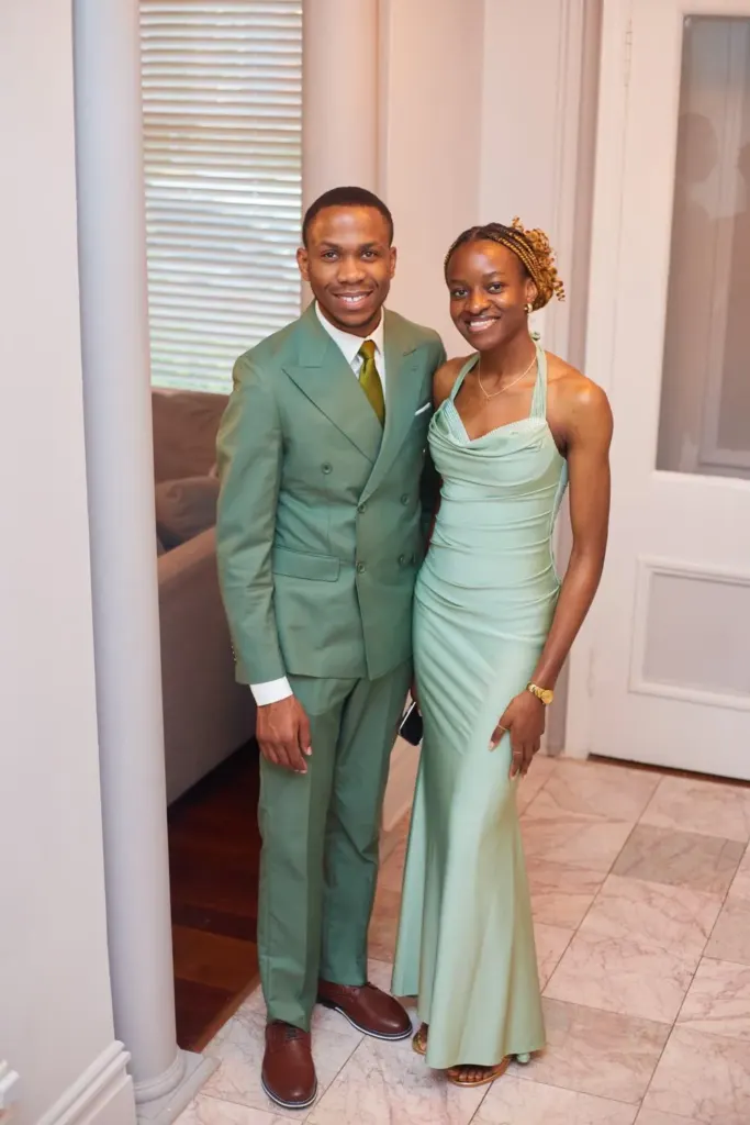Wedding party couple in matching sage suit and gown, smiling in a sunlit hallway
